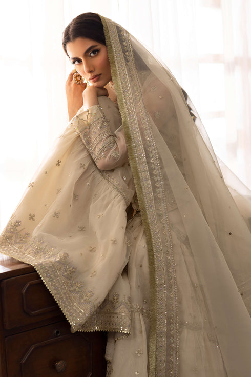 Model wearing full NAQSHI Jeena 3PC set: pearl-white organza shirt with stone boat neckline, lavender-tinged gharara, chunky tassels and embroidered sequin dupatta.